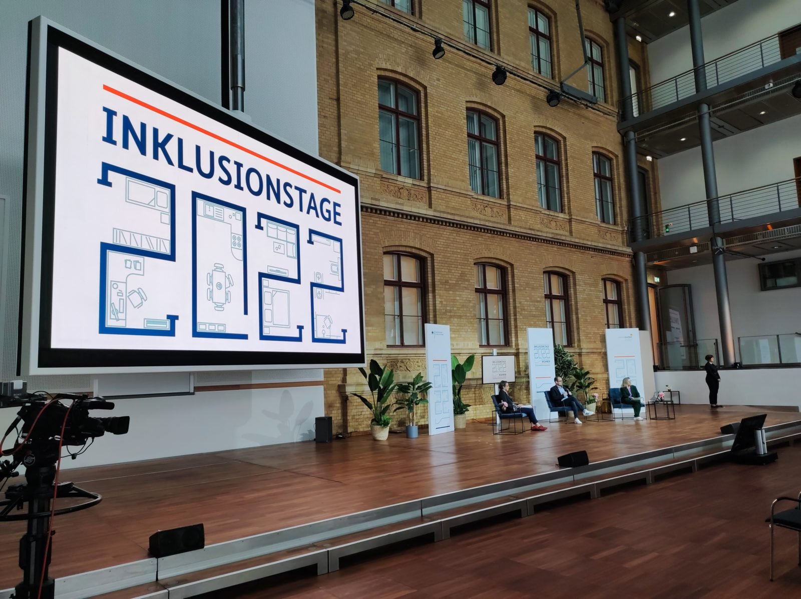 Foto des Podiums bei den Inklusionstagen. Links ein großer Bildschirm mit dem Schriftzug "Inklusionstage 2022"