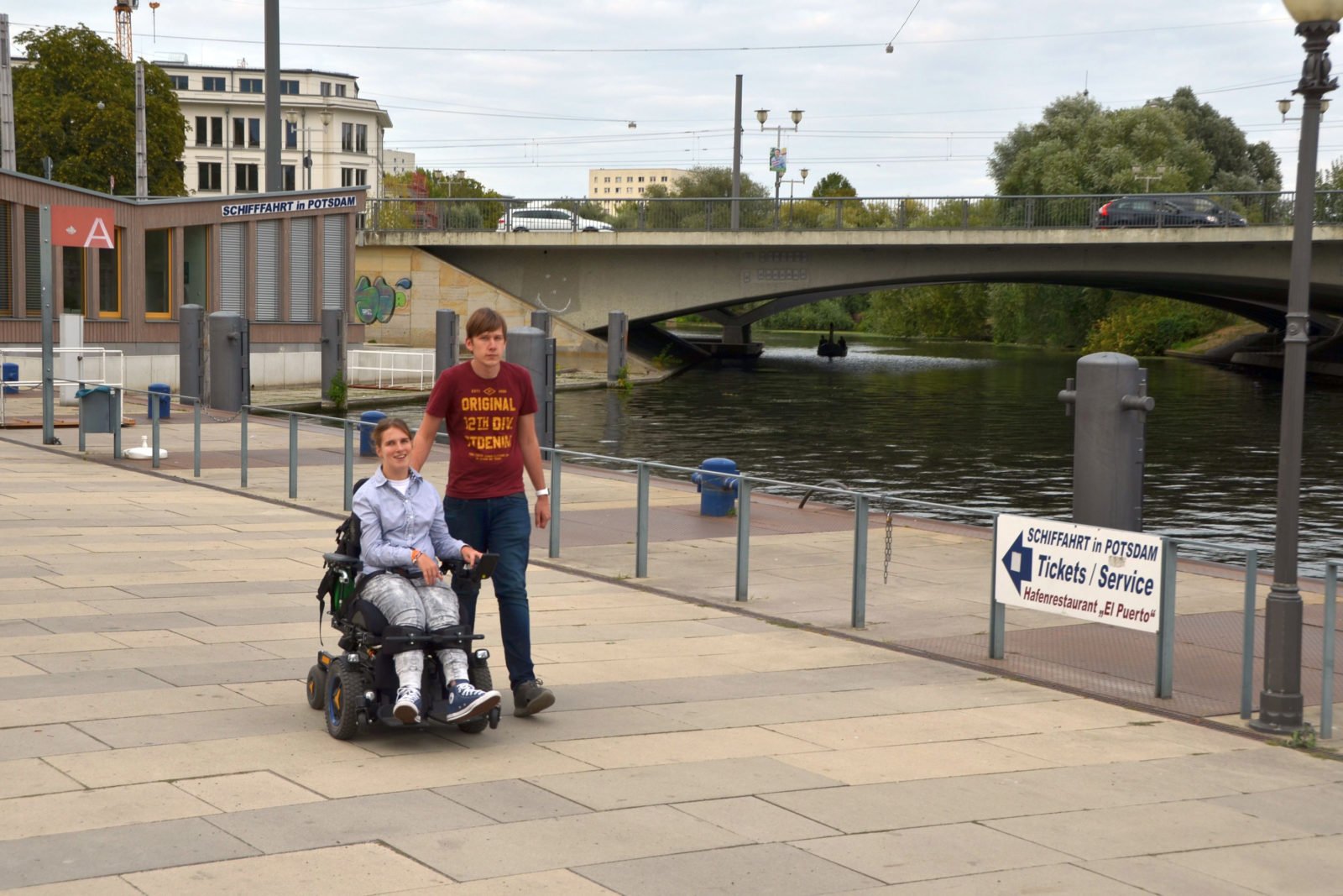 Lea Voitel und ihr Freund beim SPaziergang am Potsdamer Hafen. Sie sitzt im E-Rollstuhl, er leäuft rechts neben ihr.