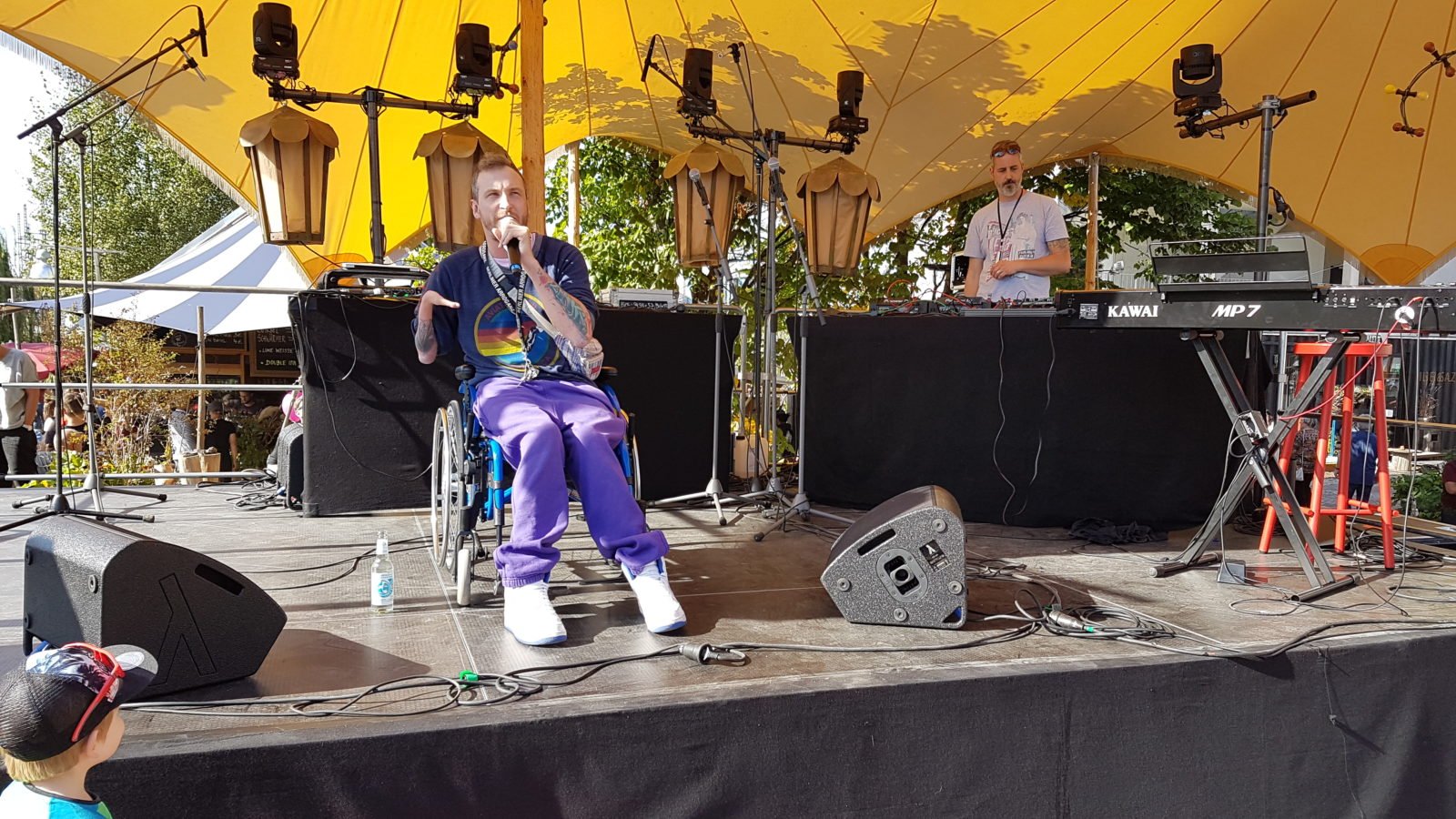 Mann im Rollstuhl singt mit Mikrofon in der Hand auf der Bühne