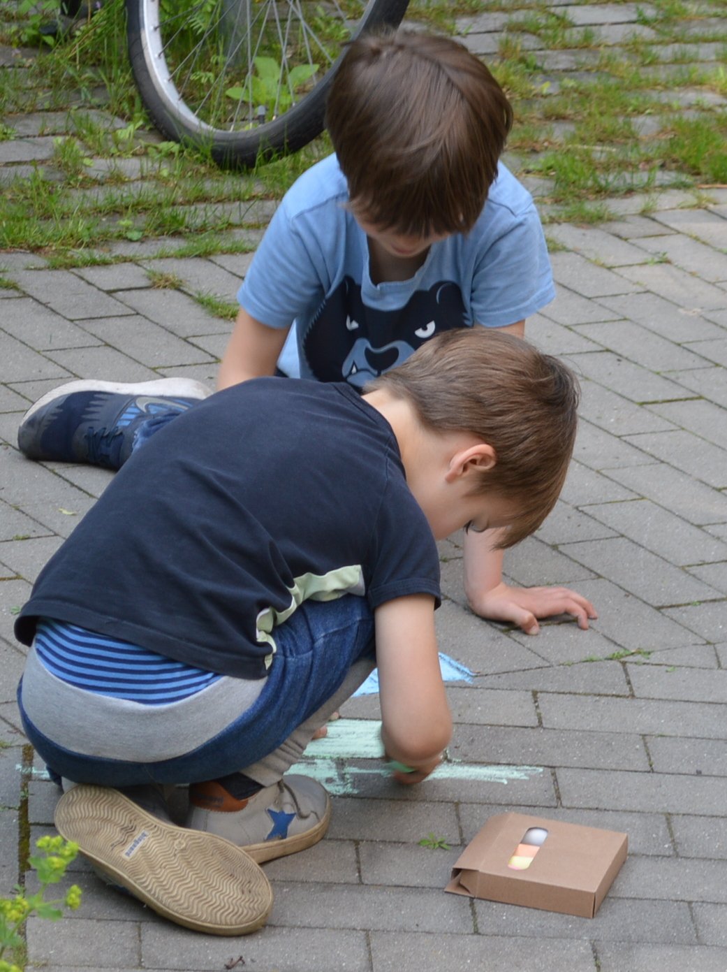 Zwei Kinder malen mit Kreide auf den Steinen vor dem Haus.