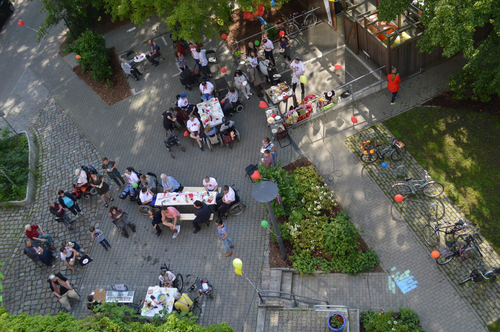 Vogelperspektive: der Tag der Nachbarn 2019 im WmI am Seelbuschring vom Balkon aus fotografiert. Leute stehen und sitzen auf dem Hof, unterhalten sich, essen Gegrilltes und haben eine gute Zeit.