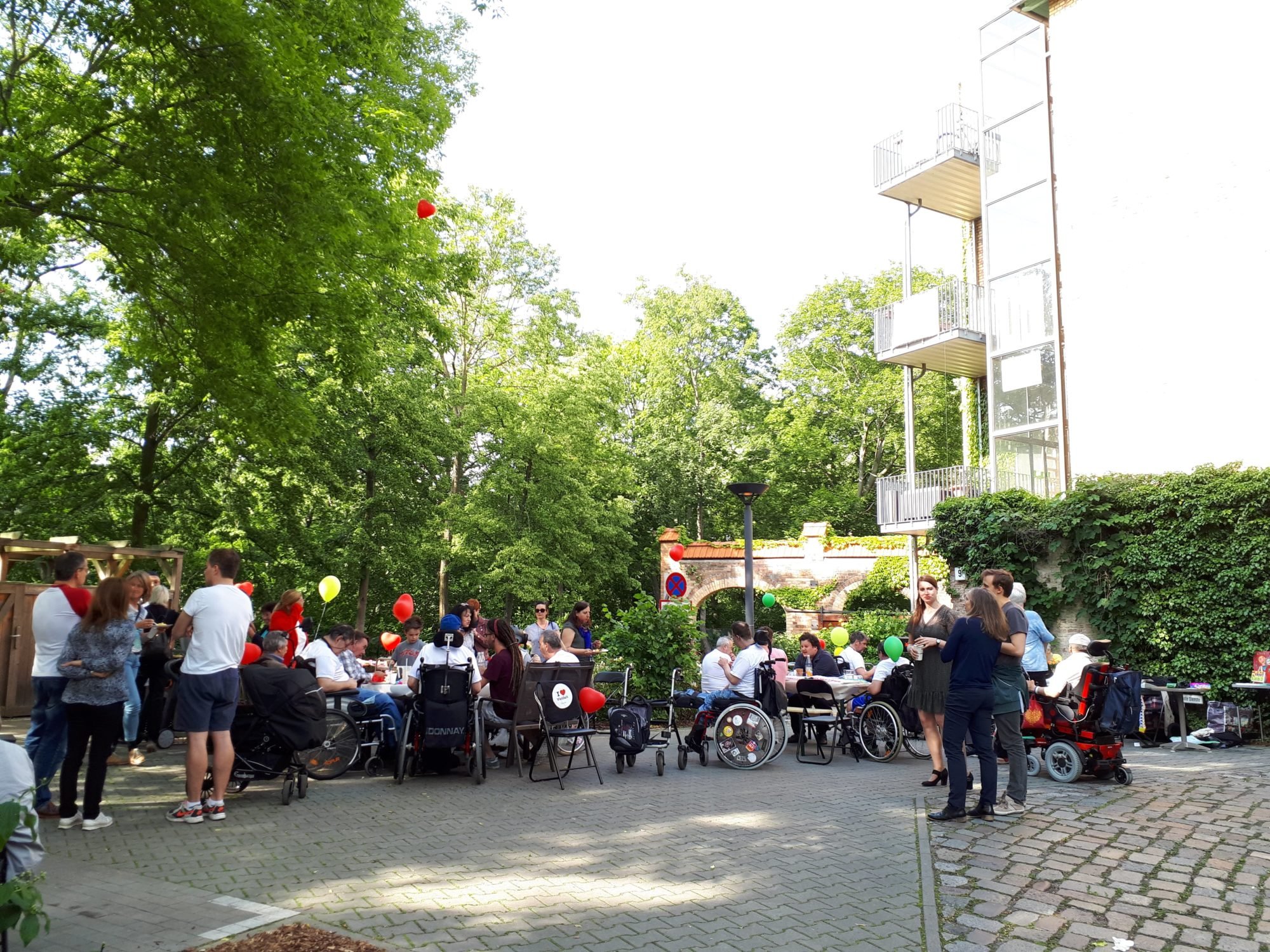 Ein schönes Fest - Blick auf das Gebäude und auf den Hof mit den Tischgruppen. Menschen sitzen und stehen hier, unterhalten sich oder essen und haben eine schöne Zeit.