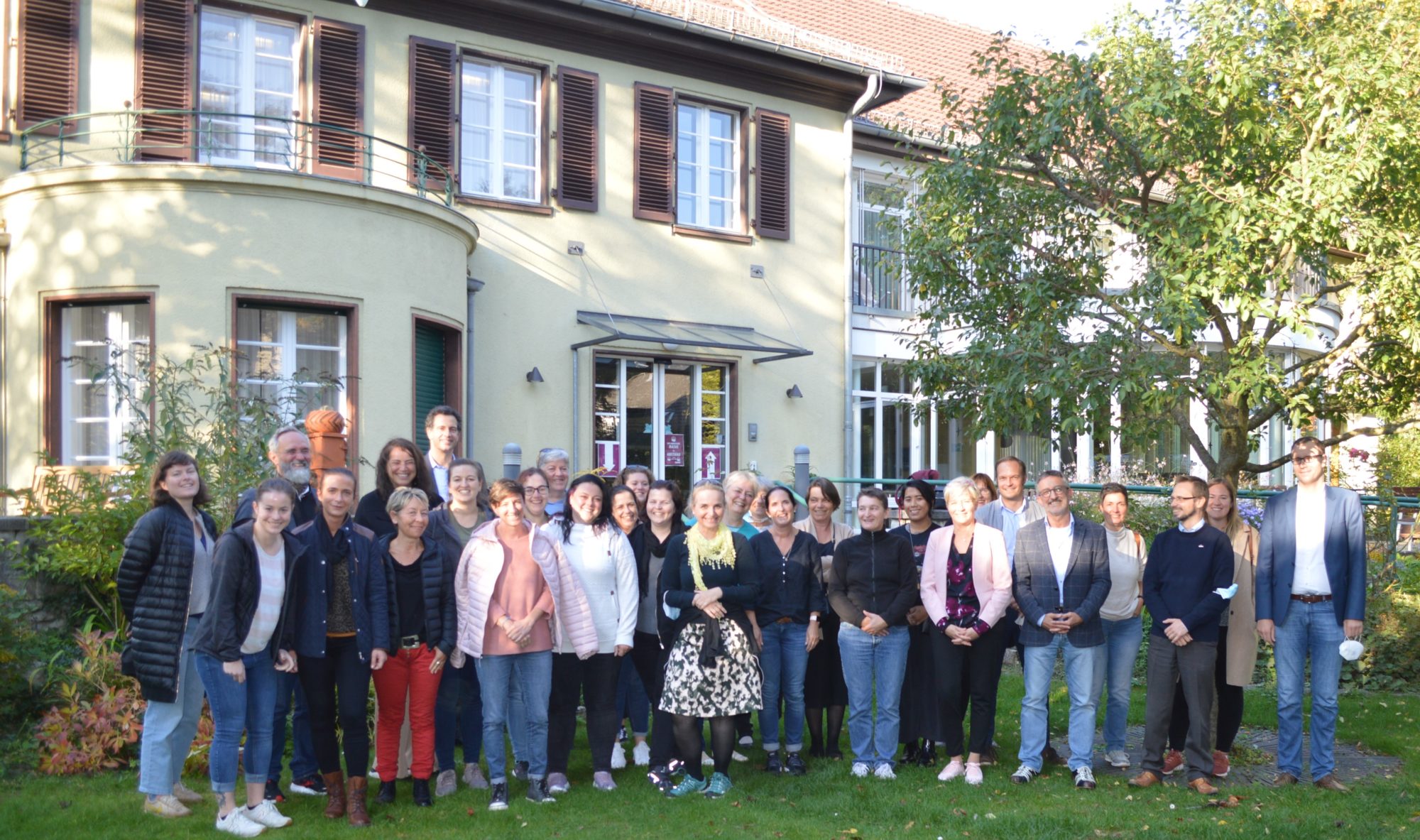 Eine Gruppe von Frauen und Männern steht auf einer Wiese vor einem Haus und posiert für einen Fotografen. Es handelt sich um Mitarbeiter der Stiftung und des Zentrum Oberwald.