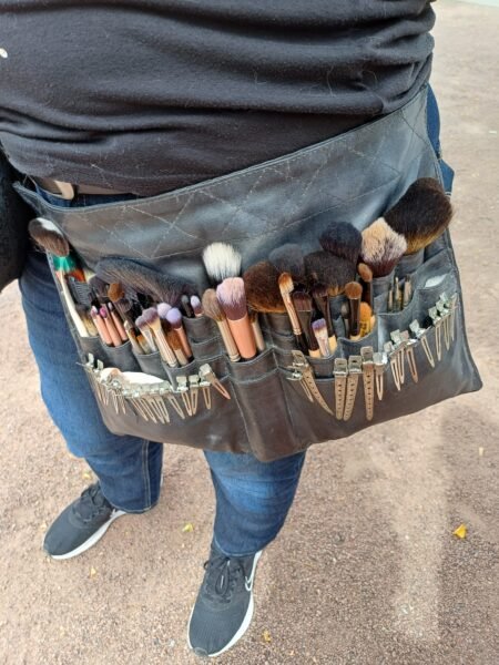 Eine Frau trägt eine Schürze in der Ihre Makeup Pinsel und Untensilien verstaut sind