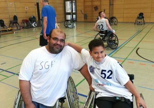 Ayman Mohsen posiert mit seinem Sohn in einer Sporthalle. Sein Sohn legt den Arm um seinen Vater - beide sitzen in einem Rollstuhl.