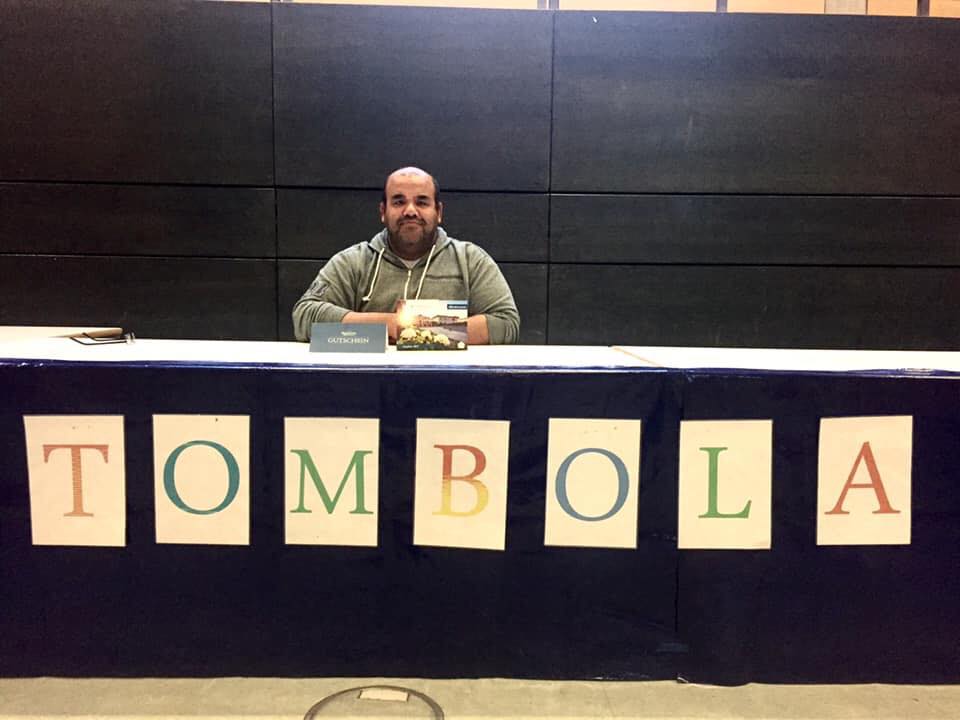 Ayman Mohsen sitzt an einem langen Tisch auf dem in Großbuchstaben Tombola steht.