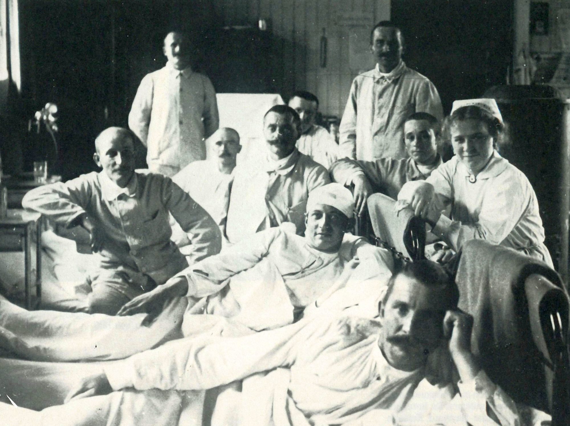 Ein historiches Schwarz-Weiß Foto: Mehrere Männer in und um ihre Betten im Vereinslazarett. Rechts im Bild auch eine Krankenschwester.