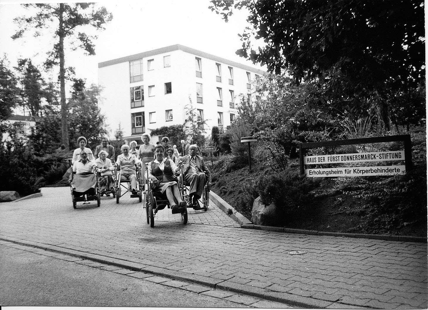 50 Jahre Heidehotel: Ein frühes Schwarz-Weiß-Foto vor dem Hotel in Bad Bevensen, davor eine Gruppe Rollstuhlfahrerinnen und fahrer.