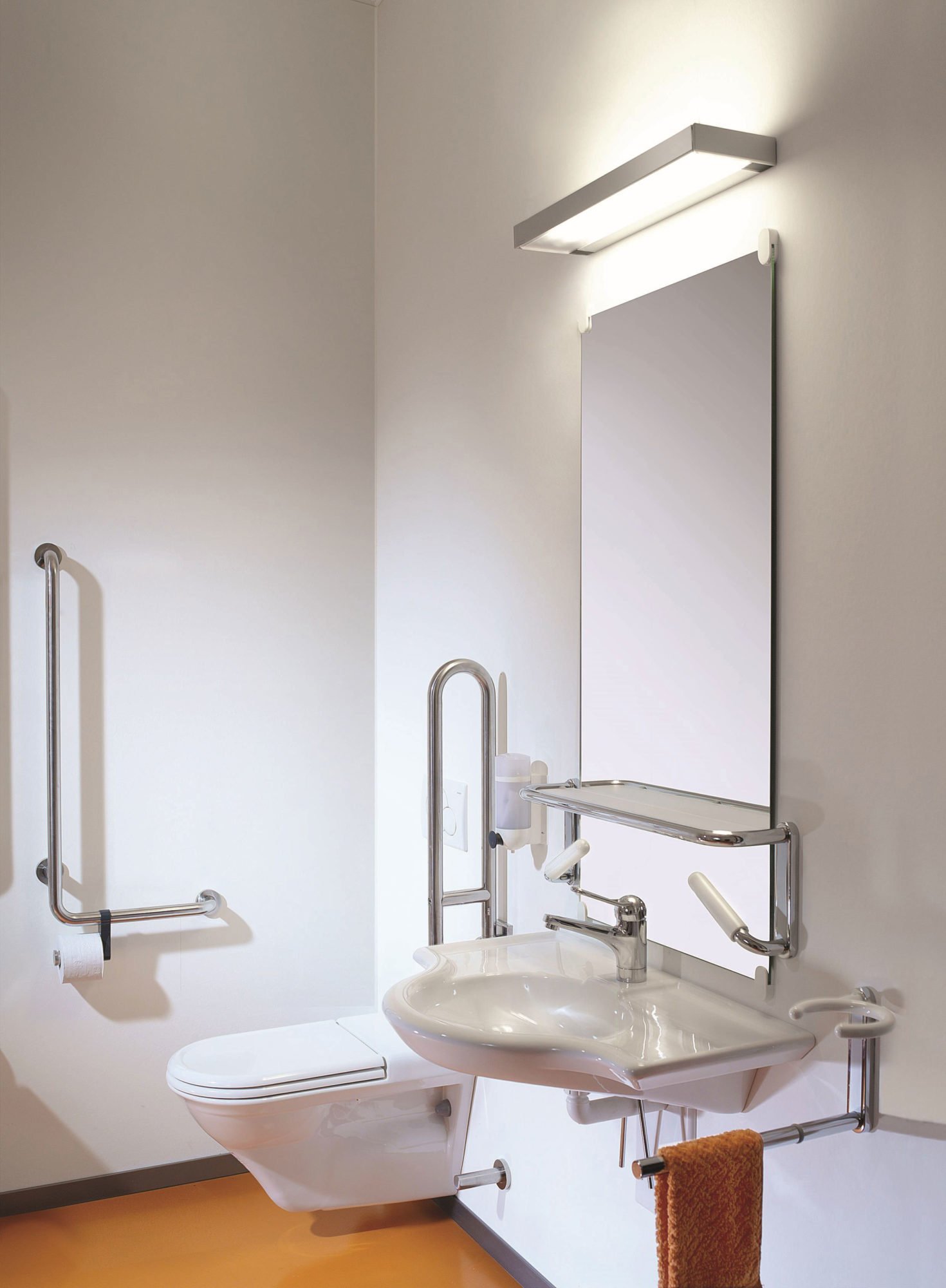 Zu sehen ist ein barrierefreies WC. Ein unterfahrbares Waschbecken und ein Spiegel mit Lampe.