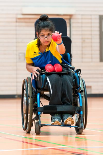 Eine junge Frau im Rolstuhl beim Boccia spielen.