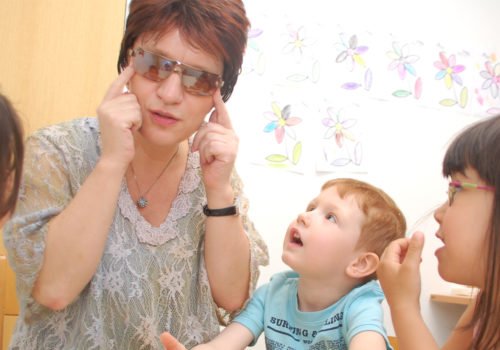 Silja Korn und mehrere Kita-Kinder sitzen zusammen. Die Kinder schauen ihre Erzieherin an.