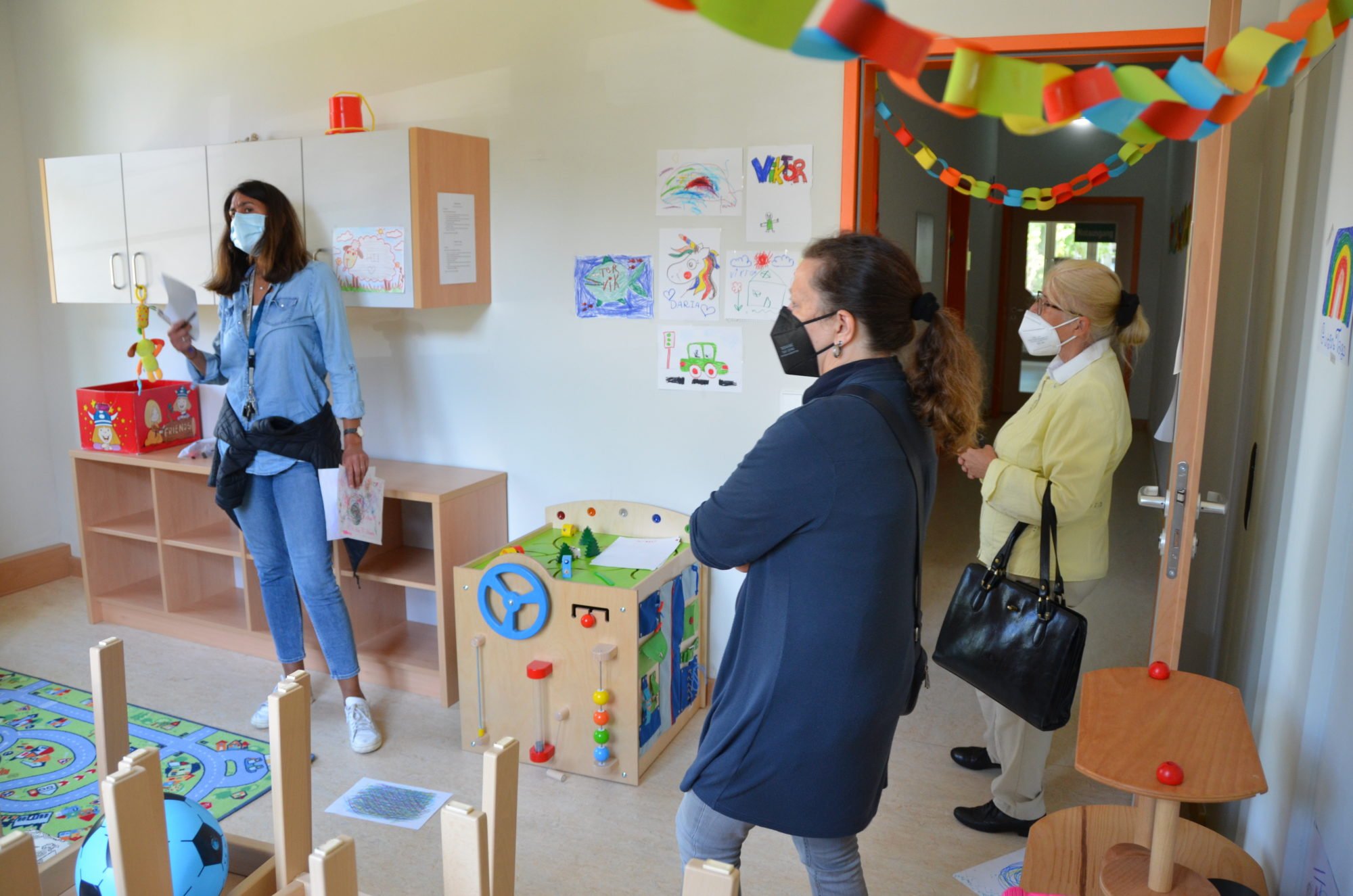 Drei Frauen bei der Hausbegehung in einem extra für Kinder mit Kindermöbeln und Spielzeug ausgestattetem Zimmer. An den Wänden hängen von den Kindern gemalte Bilder.