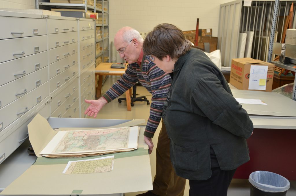 Gerd Heinemann öffnet eine Schublade des Archivschrankes und präsentiert Anke Köhler eine ca. A2 große Mappe mit unterschiedlichen Landkarten.