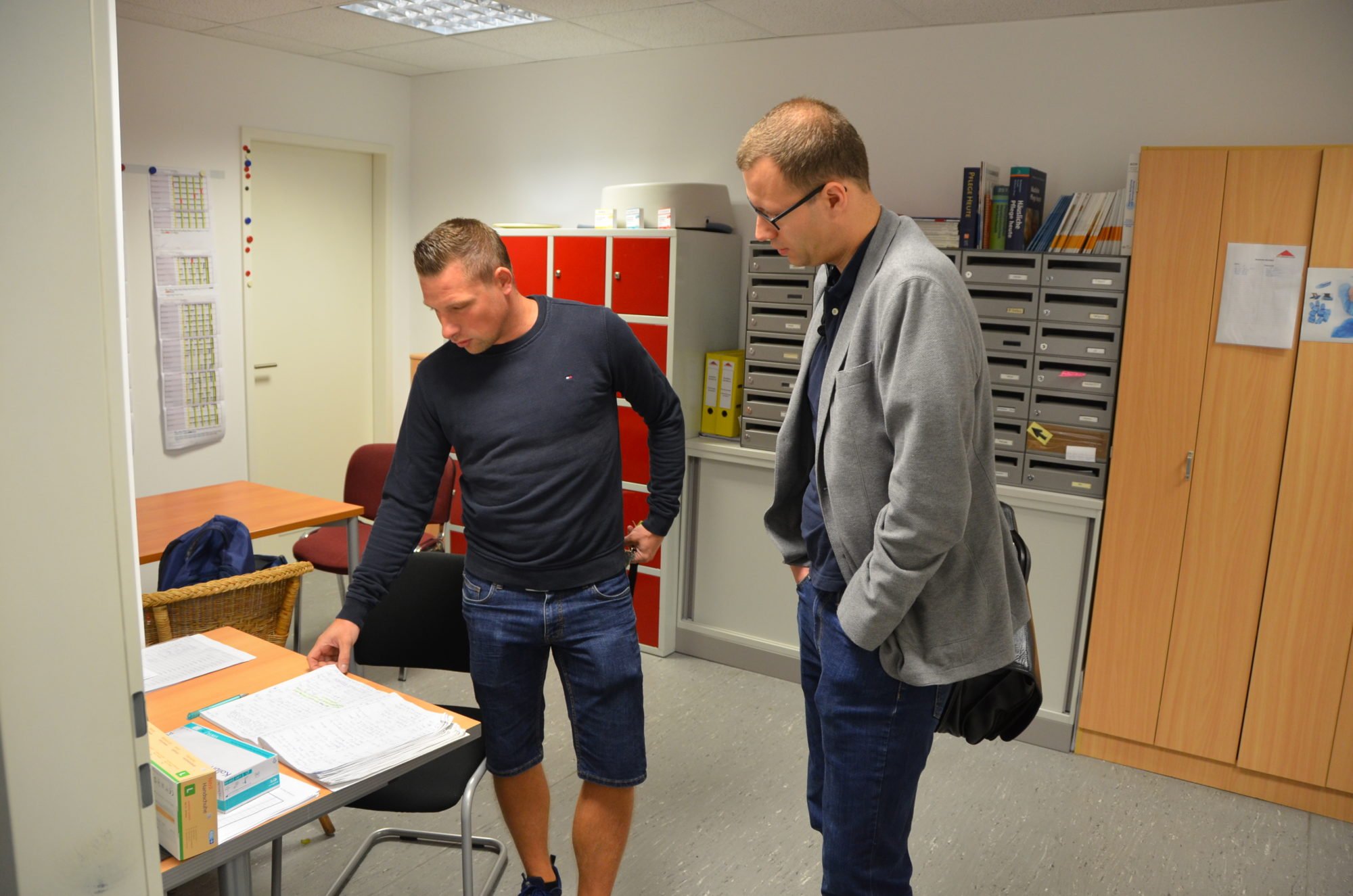 Pflegefachkraft Marco Noack im Büro des AD. Er zeigt Dr. Sebastian Weinert den Dienst- und Tourenplan.
