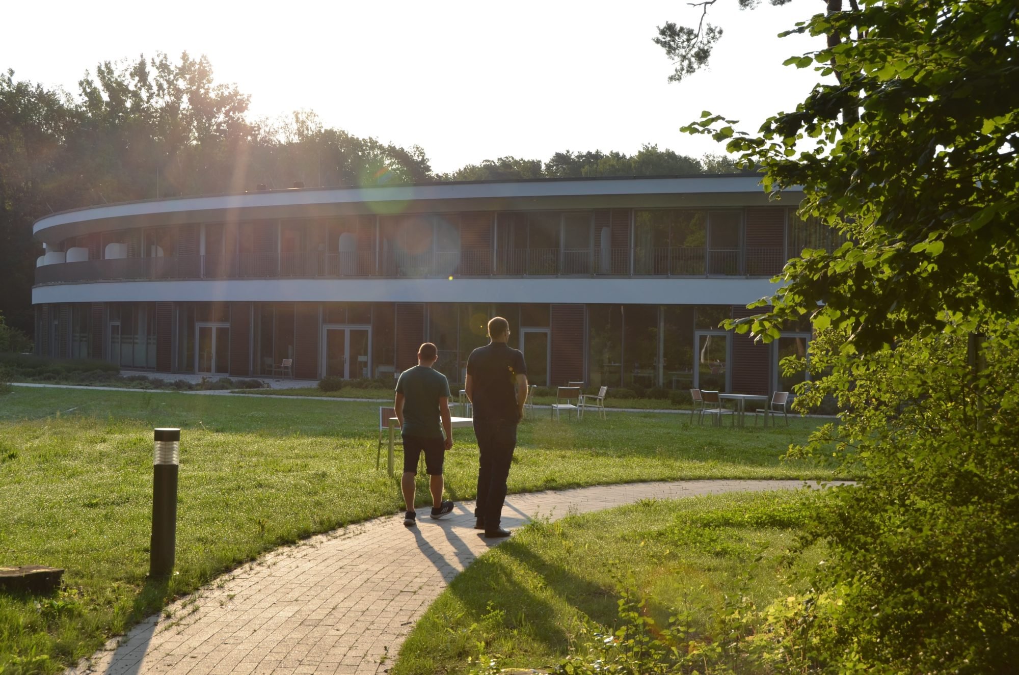 Marco Noack und Dr. Sebastian Weinert laufen auf das P.A.N. Zentrum zu. Darüber geht die Sonne auf.