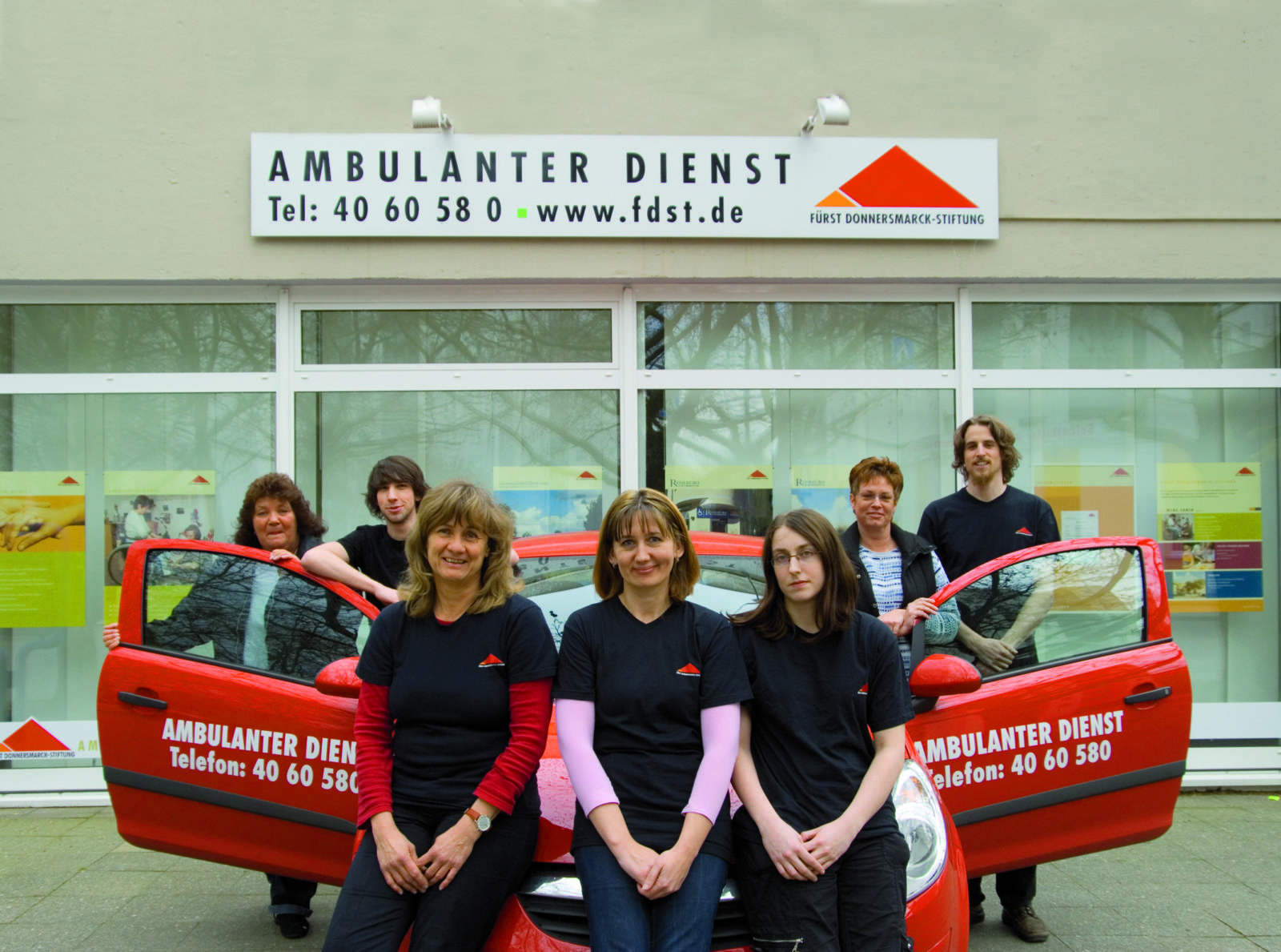 Gruppenfoto vor einem Auto und den Büros des Ambulanten Dienstes.
