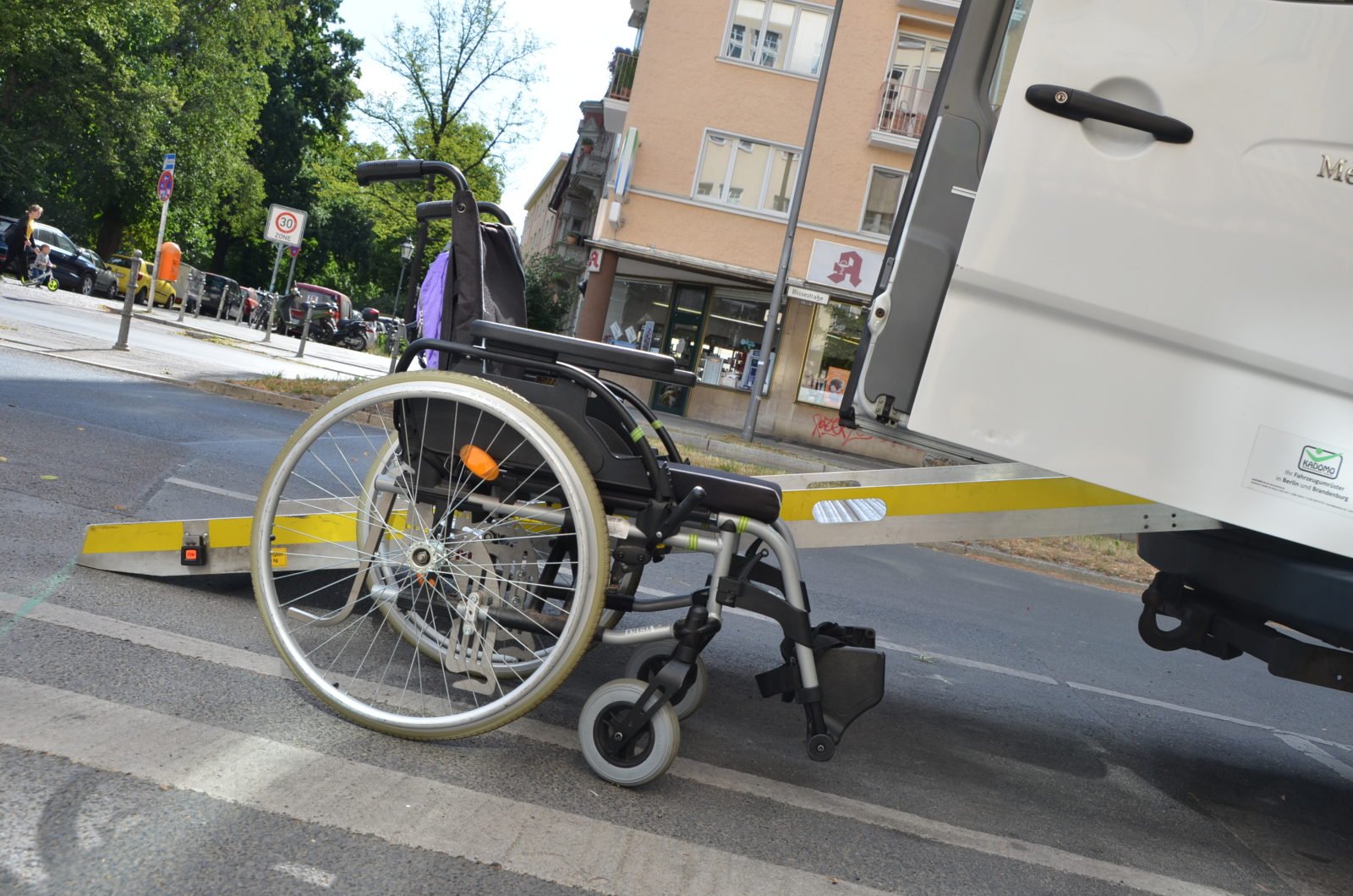 Ein leerer Rollstuhl steht vor einem Sprinter-Bus mit Rampe.