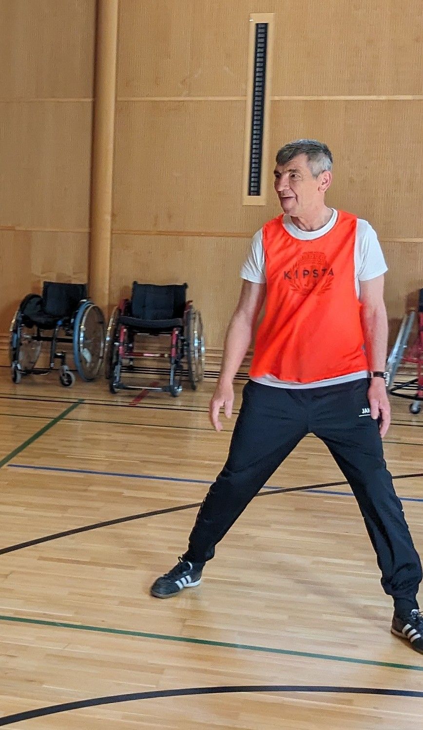 Herbert Komnik steht in der Halle, er trägt ein rotes Leibchen und beobachtet scheinbar die Szenerie außerhalb des Bildes.