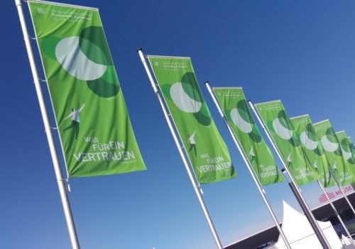 Flaggen des Kirchentages mit dem Logo, ein Mann der an Ballons wegfliegt, und dem Schriftzug "Was für ein Vertrauen".