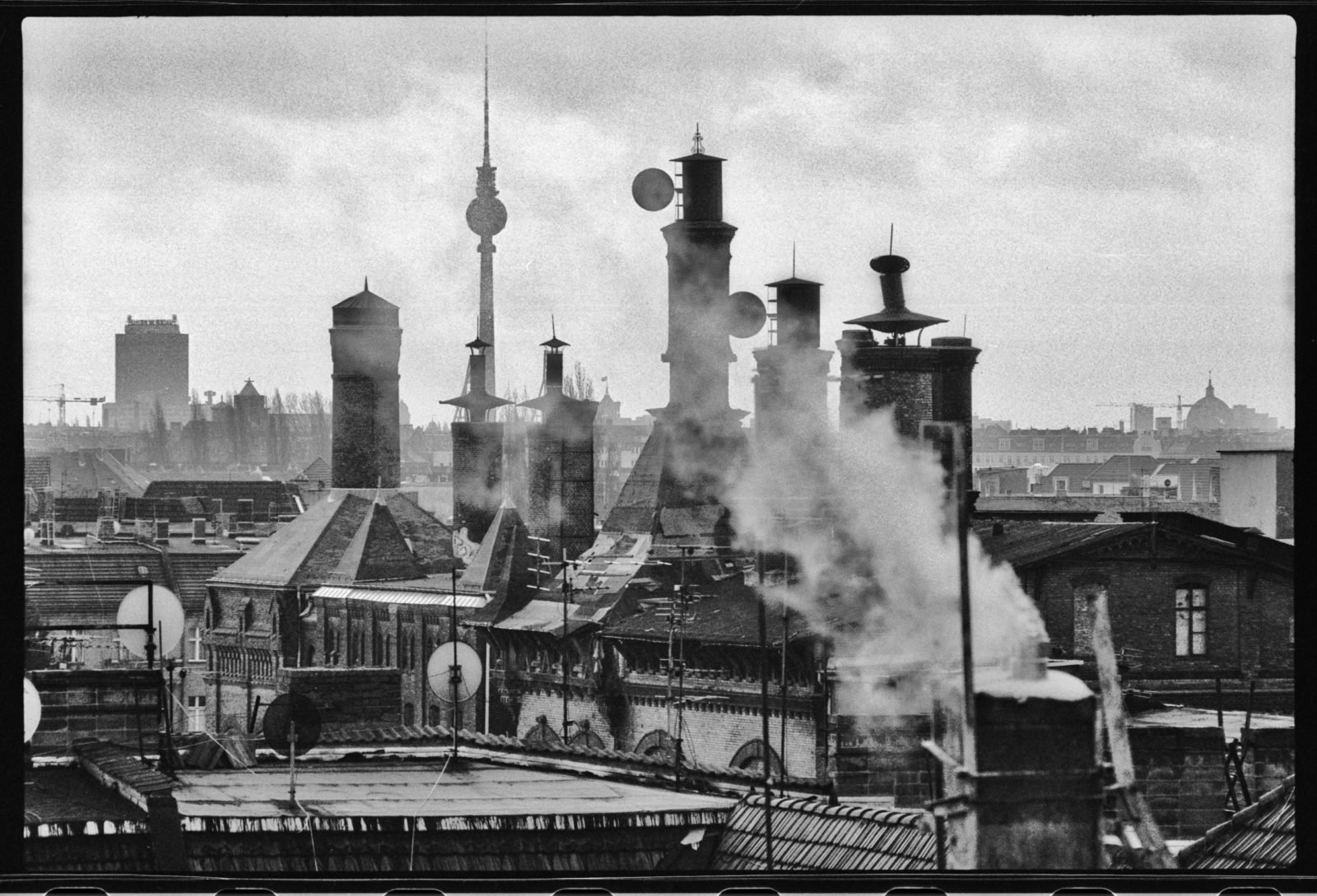 Schwarz-Weiß-Foto über den Dächern Berlins: Die Schornsteine der alten Mälzerei in Pankow sind zentral im Bild zu sehen, drumherum weitere Dächer und im Hintergrund der Fernsehturm