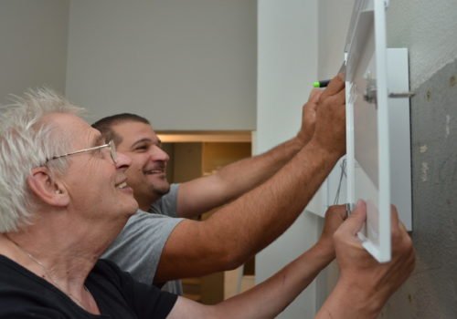 Zwei Männer bringen einen Briefkasten an der Wand an.