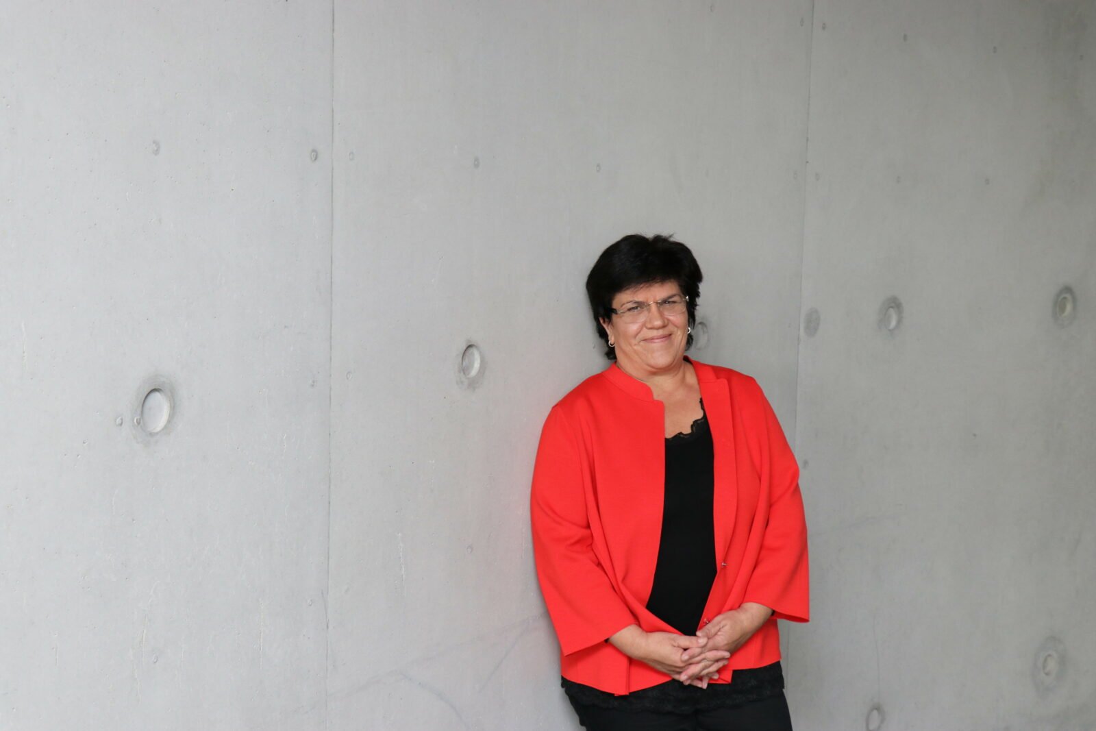 Pressefoto von Claudia Moll in rotem Blazer vor eine grauen Wand.