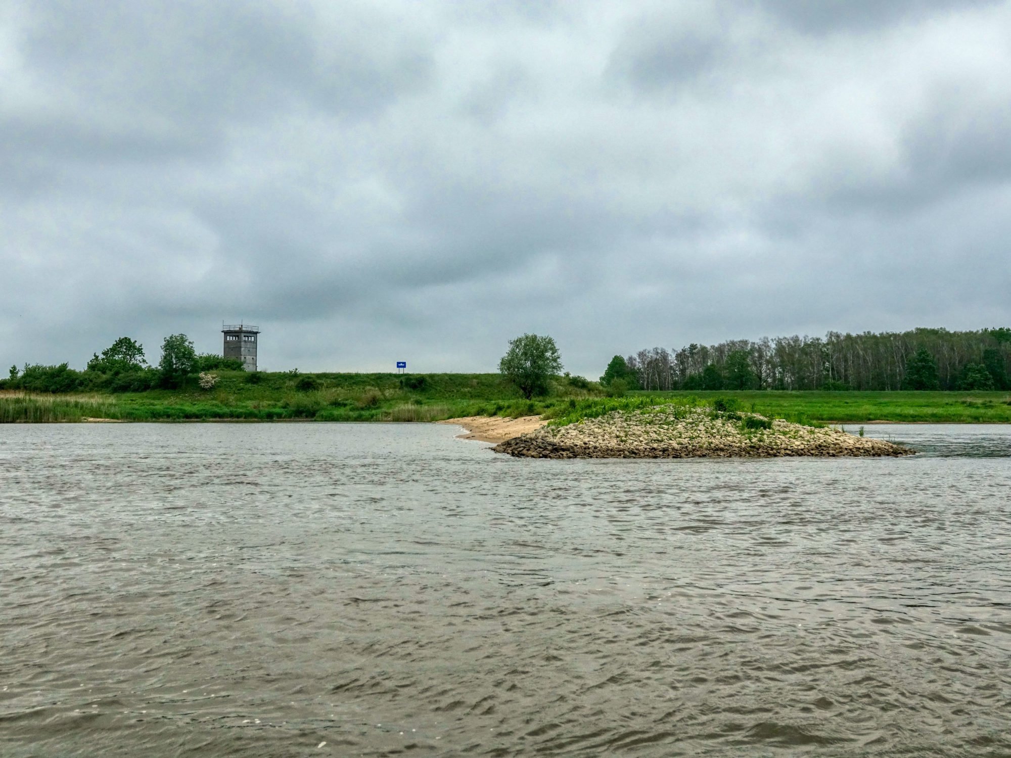 Vorne ist die Elbe zu sehen, im Hintergrund Gras und Bäume sowie ein alter Grenzwachturm.