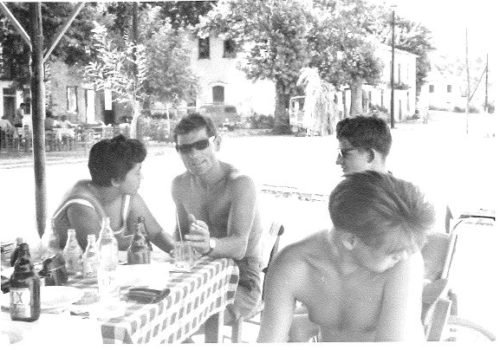 Scan einer Schwarzweißfotografie: drei Männer, alle oberkörperfrei und einer davon im Rollstuhl sitzend, und eine Frau sitzen gemeinsam an einem Tisch.