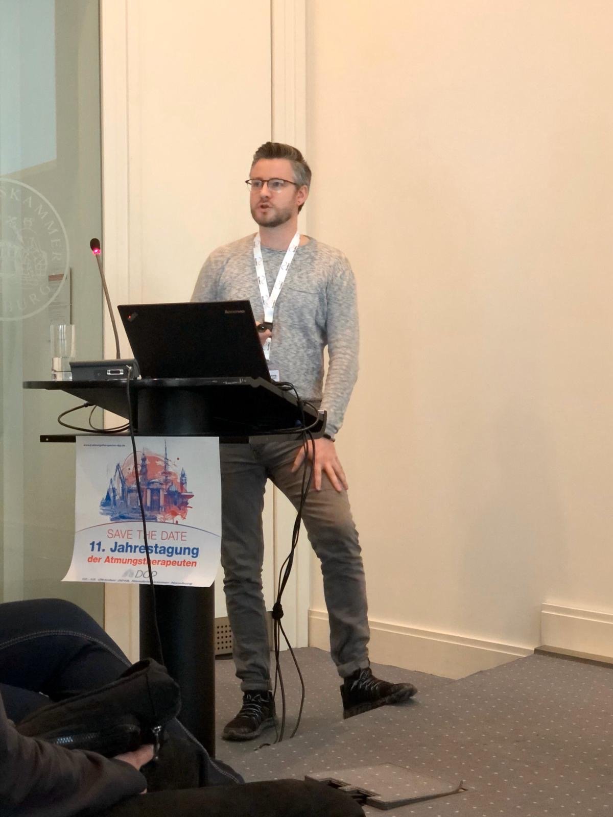 Philipp Gutschmidt hinter einem Rednerpult, auf dem das Logo des AT-Kongress zu sehen ist.