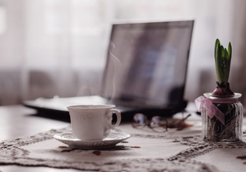 Ein Laptop und eine Tasse Kaffee auf einem Tisch mit Tischdecke.