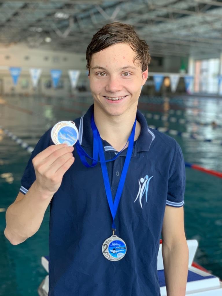 Jan Schreiber vor einem Schwimmbecken. Er hält eine Medaille in der Hand und lächelt in die Kamera.