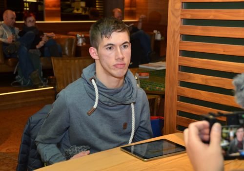 Jasper Dombrowski sitzt an einem Tisch in einem Café er wird gefilmt, das Display der Kamera ist im rechten unteren Bildrand zu erkennen, Jasper blickt direkt in die Kamera.