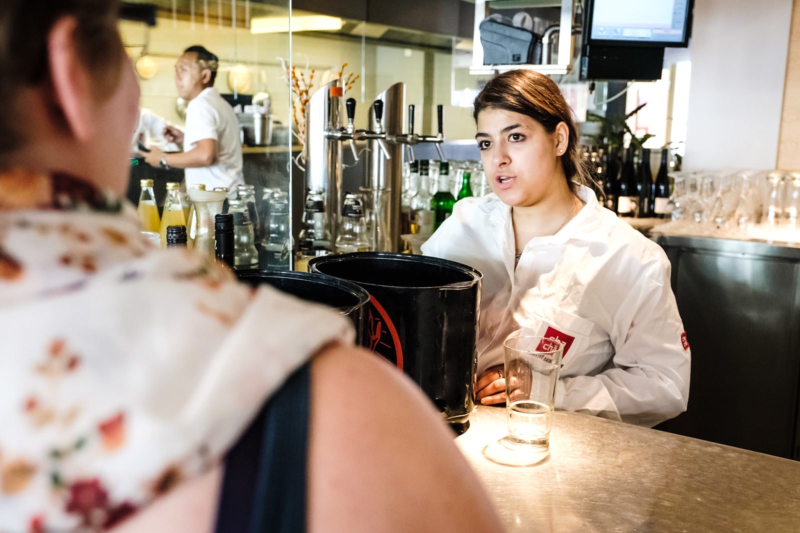 Eine junge Frau steht in einem Restaurant hinter der Bar und bedient einen Gast.