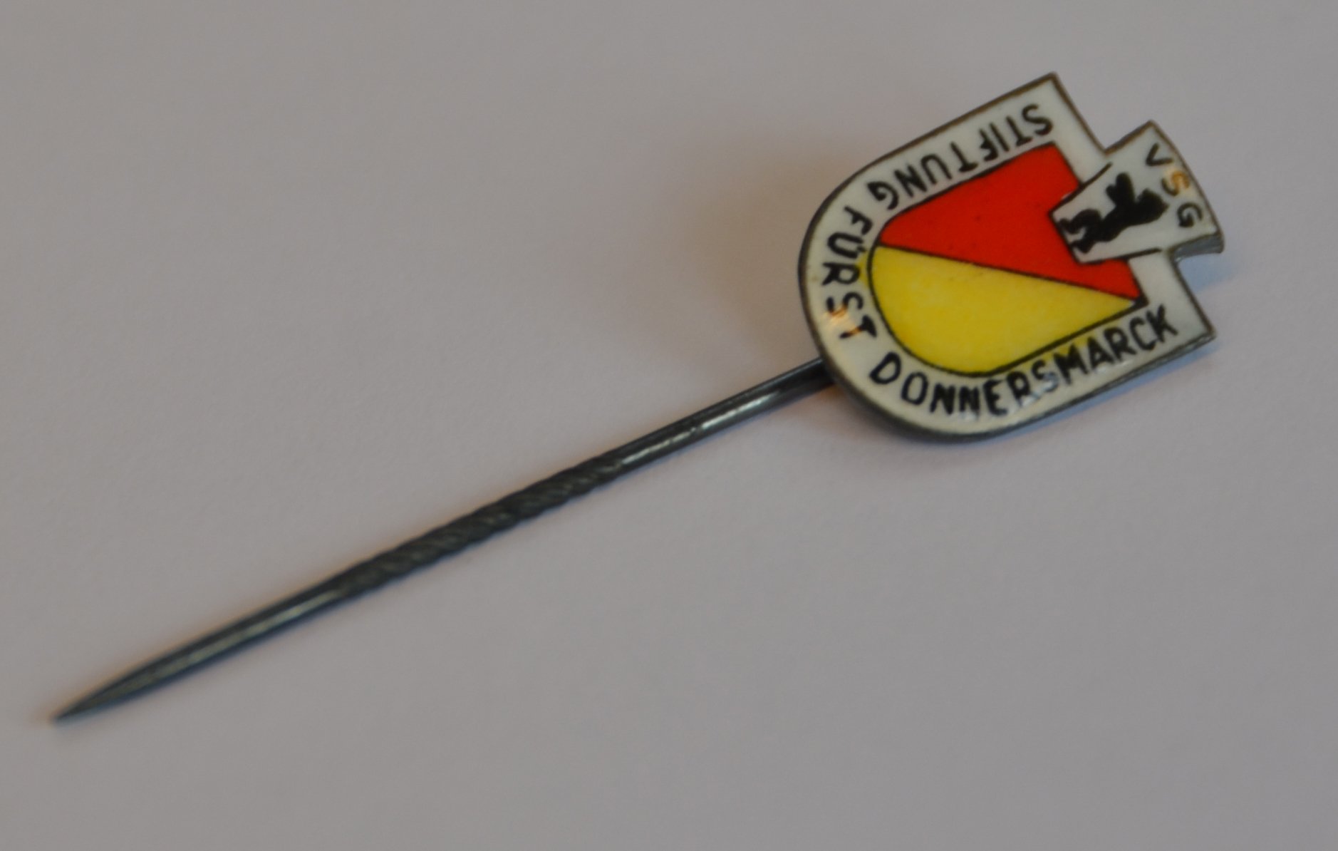 Eine Anstecknadel mit dem selben Logo des Abzeichens.