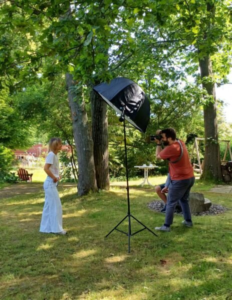 Ein Fotograf fotografiert eine Frau im Grünen zwischen ihnen steht ein großes Licht