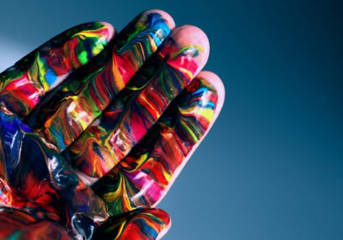 eine bunt angemalte Hand schiebt sich vom linken unteren Bildrand in den Fokus
