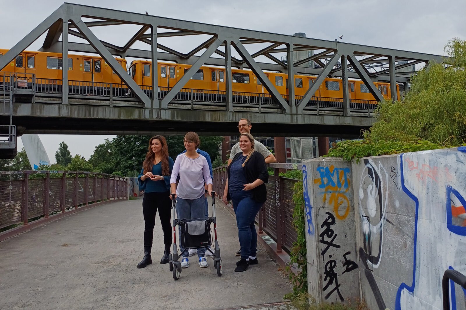Drei Frauen und ein Mann stehen vor einer Bahnbrücke und posieren für ein Foto