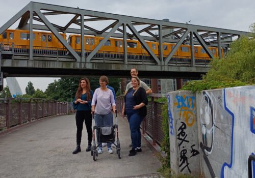 Drei Frauen und ein Mann stehen vor einer Bahnbrücke und posieren für ein Foto